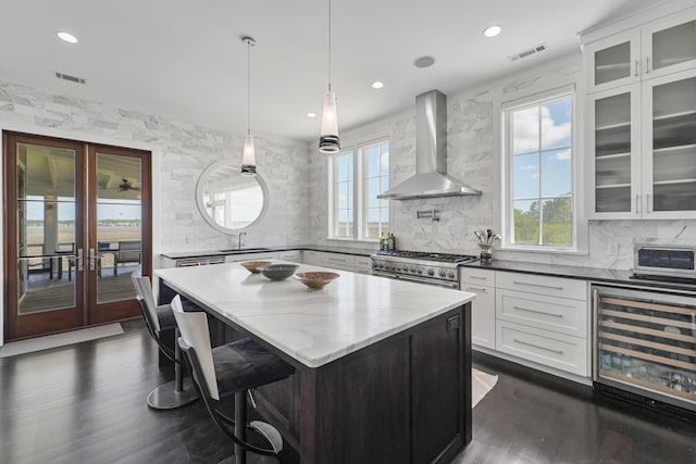 kitchen featuring wall chimney range hood, a sink, tasteful backsplash, wine cooler, and visible vents