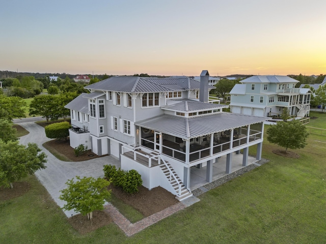 back of house at dusk featuring stairs, an attached garage, a sunroom, driveway, and metal roof