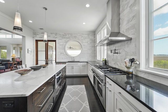kitchen featuring plenty of natural light, dark stone countertops, appliances with stainless steel finishes, and wall chimney range hood