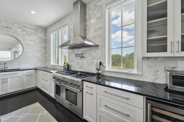 kitchen featuring beverage cooler, wall chimney range hood, plenty of natural light, range with two ovens, and a sink