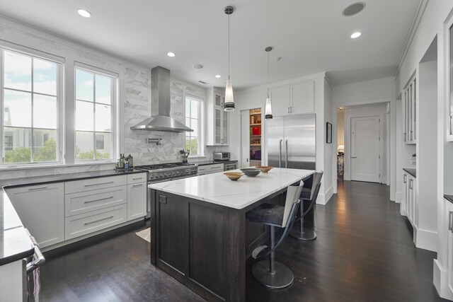 kitchen with wall chimney range hood, high quality appliances, dark wood-style flooring, and a center island