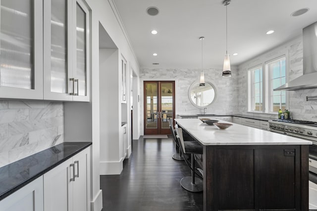 kitchen with high end stainless steel range, decorative backsplash, plenty of natural light, and wall chimney exhaust hood