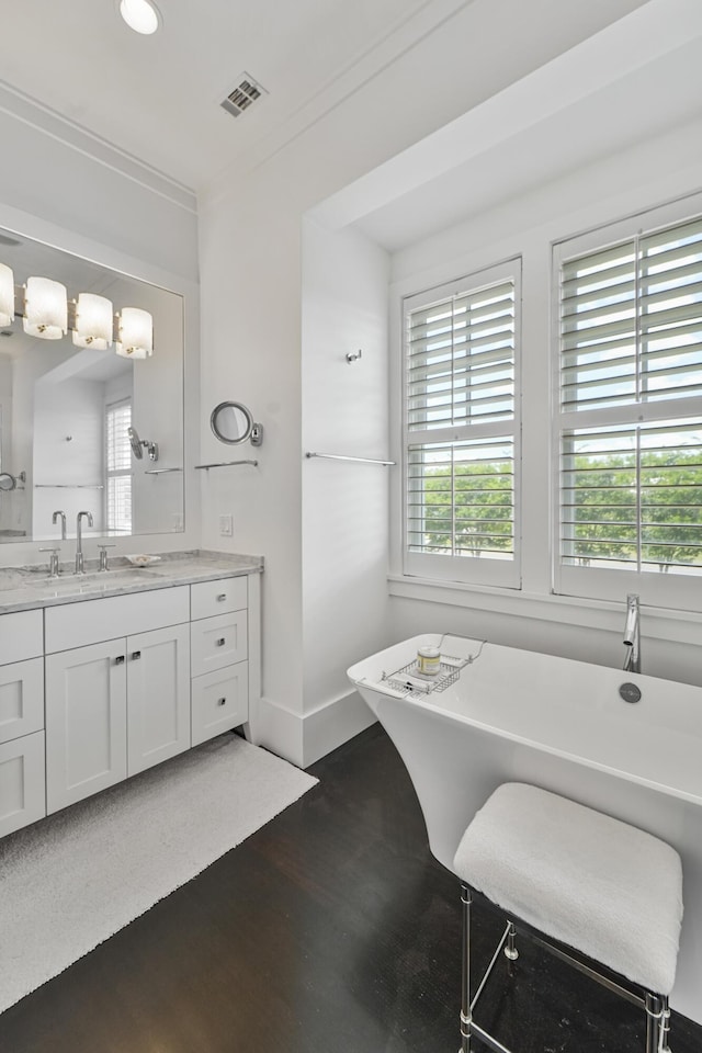 bathroom with visible vents, a freestanding bath, wood finished floors, baseboards, and vanity