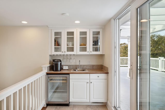 bar with beverage cooler, white cabinetry, sink, and light tile flooring