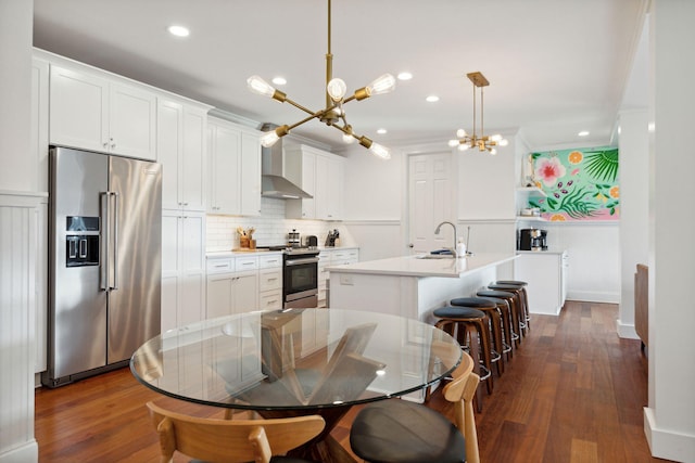 kitchen with hanging light fixtures, dark wood-type flooring, an inviting chandelier, appliances with stainless steel finishes, and an island with sink