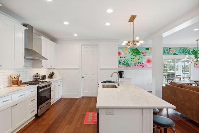 kitchen featuring white cabinets, sink, wall chimney exhaust hood, hanging light fixtures, and stainless steel gas range oven