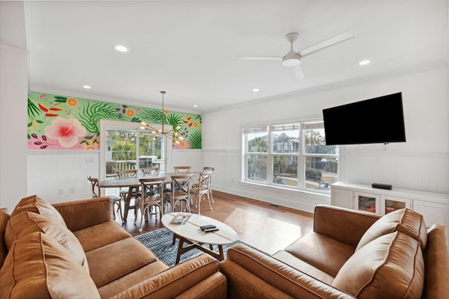 living room with crown molding, ceiling fan with notable chandelier, a wealth of natural light, and light wood-type flooring