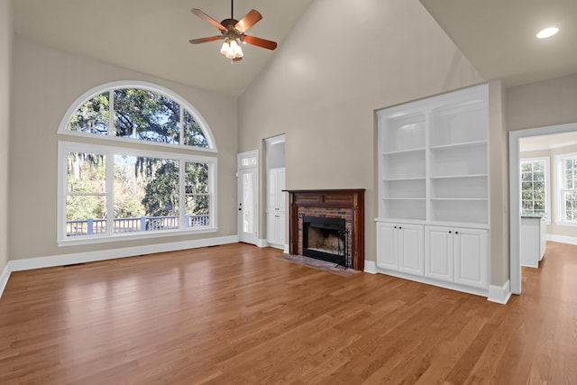 unfurnished living room with wood-type flooring, high vaulted ceiling, ceiling fan, and a fireplace