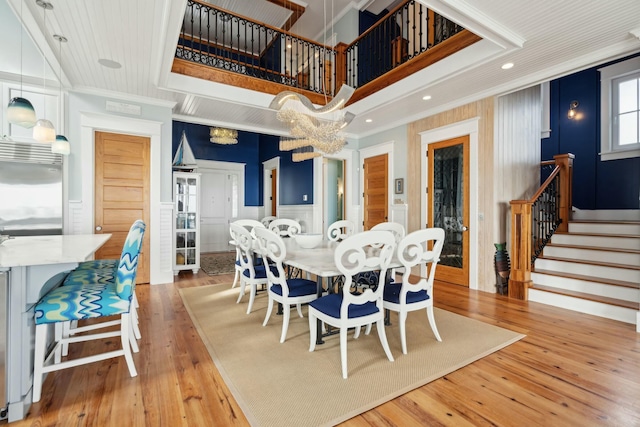 dining space with light wood-type flooring, wainscoting, crown molding, and stairway