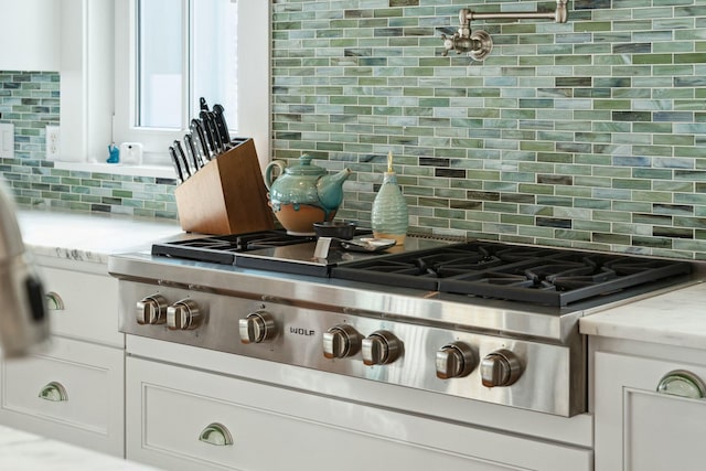 details featuring light stone counters, white cabinetry, stainless steel gas stovetop, and backsplash