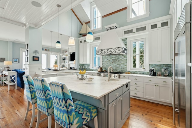 kitchen featuring a wainscoted wall, light wood-style flooring, a kitchen island with sink, gray cabinets, and premium range hood