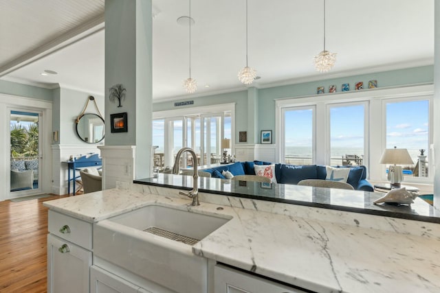 kitchen with open floor plan, wood finished floors, light stone countertops, crown molding, and a sink