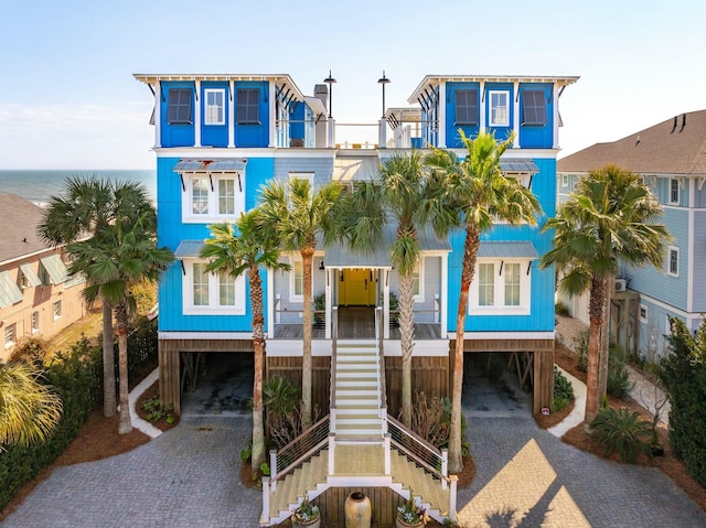 coastal inspired home featuring stairs, a carport, decorative driveway, and a balcony