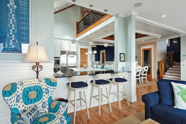 kitchen featuring stainless steel appliances, a high ceiling, light wood-style floors, open floor plan, and a kitchen bar