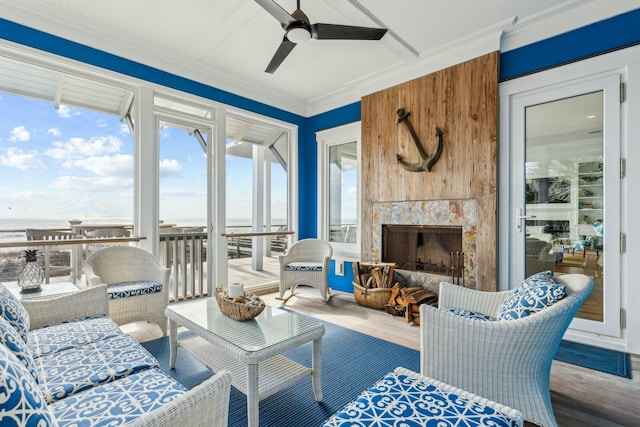 living area featuring a fireplace, wood finished floors, a ceiling fan, and crown molding