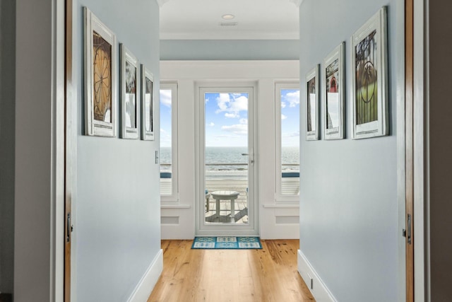 doorway to outside with light wood-style floors, a water view, ornamental molding, and baseboards