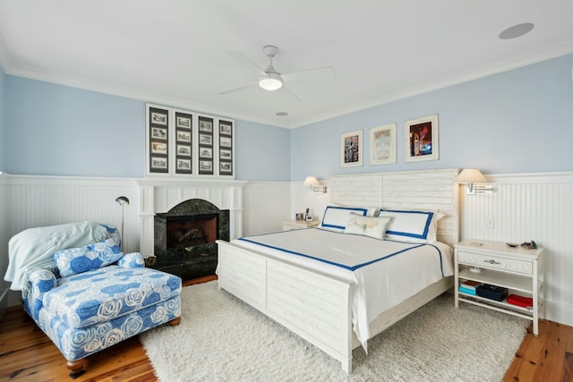 bedroom featuring a wainscoted wall, crown molding, a fireplace, and wood finished floors