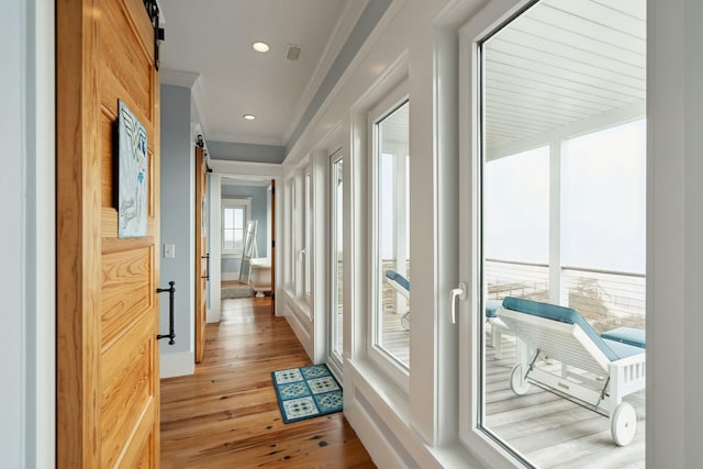 corridor with crown molding, light wood finished floors, recessed lighting, visible vents, and a barn door