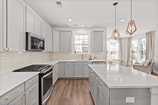 kitchen with gray cabinetry, hanging light fixtures, sink, light wood-type flooring, and appliances with stainless steel finishes