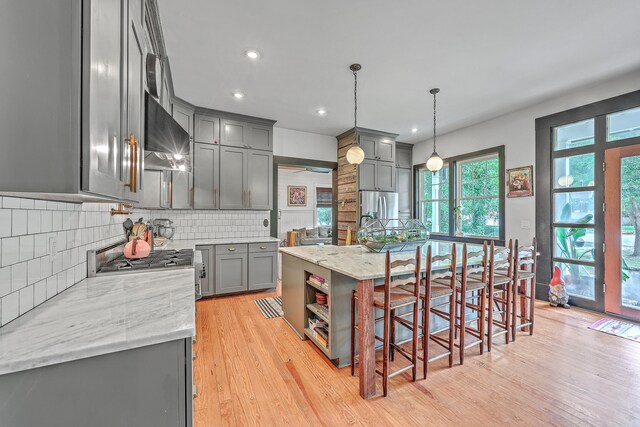 kitchen with gray cabinets, light hardwood / wood-style flooring, light stone countertops, hanging light fixtures, and a center island with sink