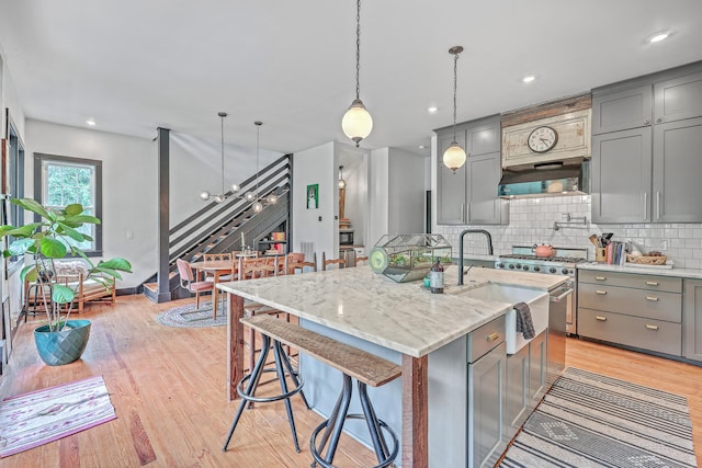 kitchen featuring a kitchen island with sink, hanging light fixtures, sink, and light hardwood / wood-style floors