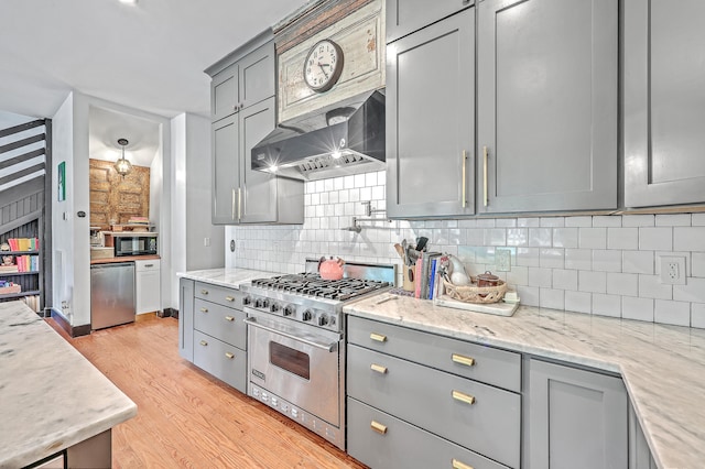 kitchen featuring light wood-type flooring, appliances with stainless steel finishes, light stone counters, gray cabinets, and decorative backsplash