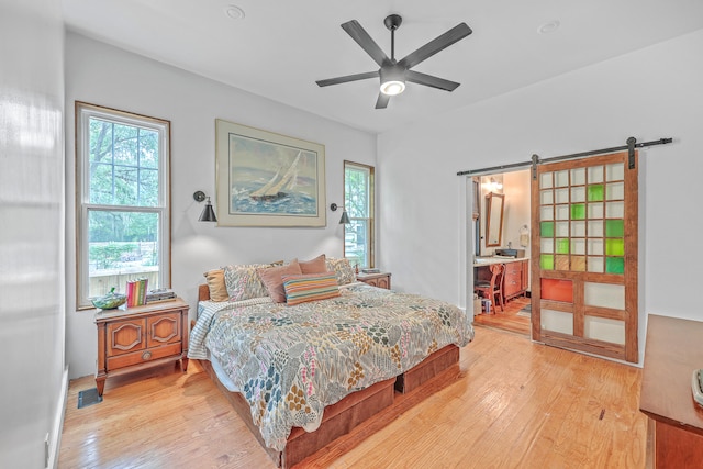 bedroom featuring a barn door, ceiling fan, light wood-type flooring, and connected bathroom