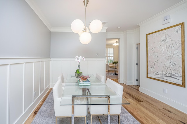 dining area with a chandelier, a wainscoted wall, ornamental molding, and wood finished floors