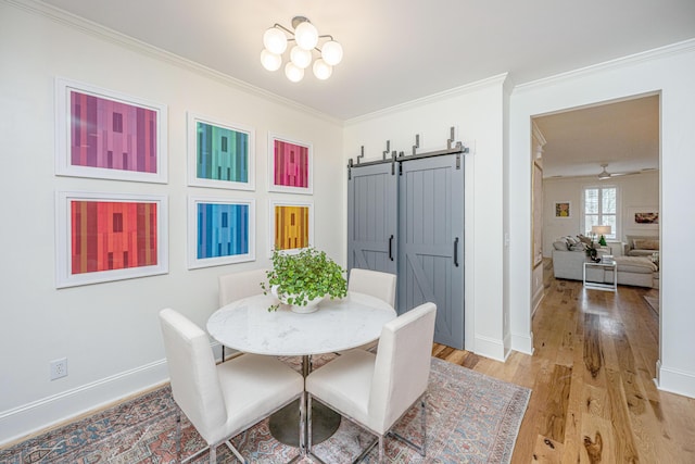 dining space featuring a barn door, baseboards, light wood-style floors, and ornamental molding