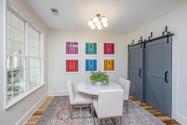 dining room with visible vents, baseboards, a barn door, ornamental molding, and light wood-style floors