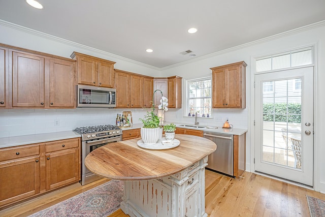 kitchen with tasteful backsplash, light countertops, ornamental molding, light wood-style floors, and stainless steel appliances