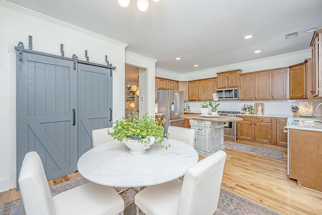 dining space featuring a barn door, light wood-style floors, visible vents, and ornamental molding