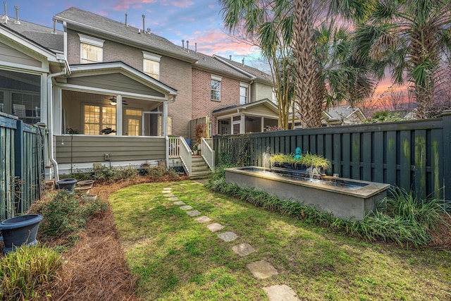 yard at dusk featuring a fenced backyard and a sunroom