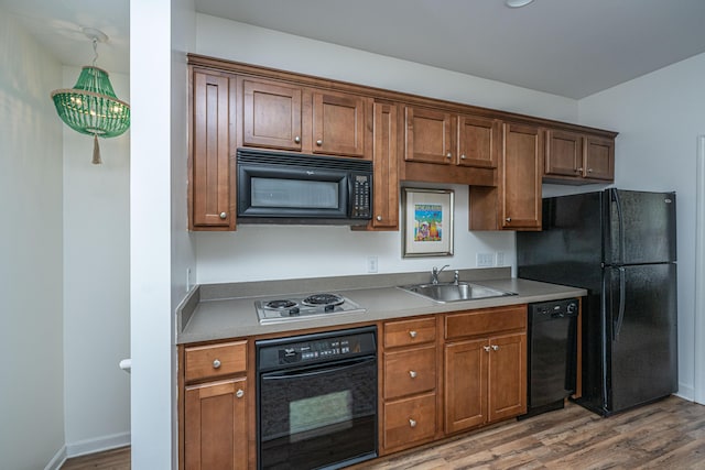 kitchen featuring black appliances, a sink, wood finished floors, brown cabinetry, and baseboards