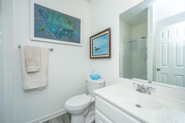 bathroom with toilet, wood finished floors, tiled shower, baseboards, and vanity