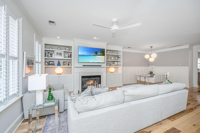 living area featuring visible vents, ceiling fan, light wood-type flooring, ornamental molding, and a glass covered fireplace