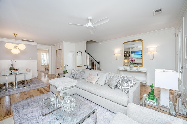 living room with visible vents, light wood-style flooring, a ceiling fan, crown molding, and stairs