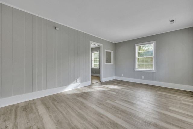 empty room with wood walls, light hardwood / wood-style flooring, and crown molding