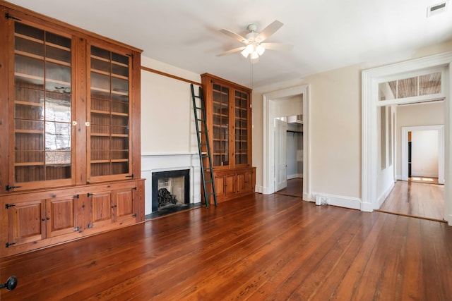 unfurnished living room with hardwood / wood-style floors, visible vents, a ceiling fan, baseboards, and a fireplace with flush hearth