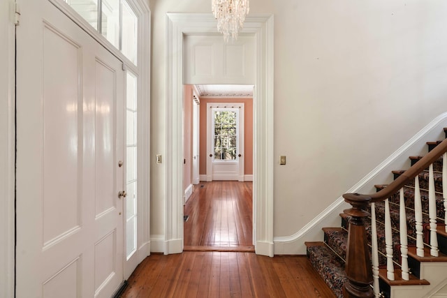 foyer entrance with stairway, an inviting chandelier, hardwood / wood-style flooring, and baseboards