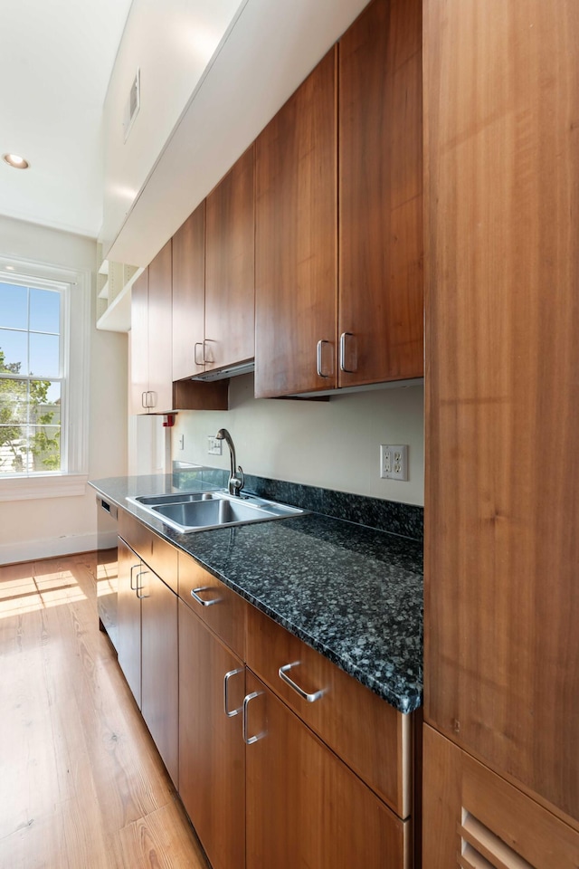 kitchen with a sink, dark stone counters, light wood-type flooring, visible vents, and baseboards