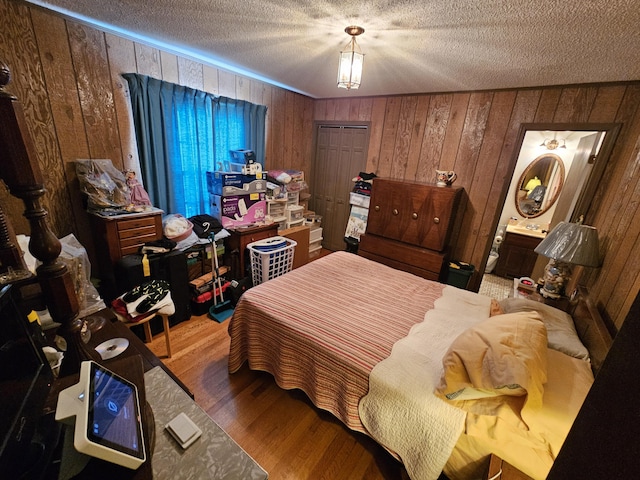 bedroom with wooden walls, ensuite bath, a textured ceiling, and wood finished floors