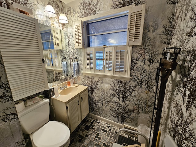 bathroom featuring baseboards, vanity, toilet, and wallpapered walls