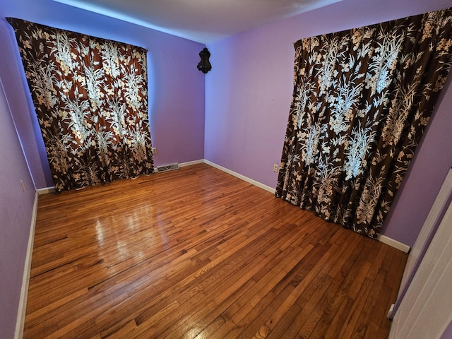 spare room with baseboards, visible vents, and wood finished floors