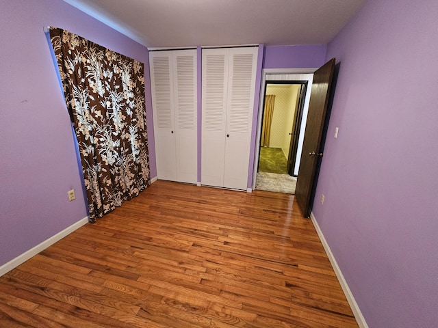 unfurnished bedroom featuring baseboards, two closets, and wood finished floors