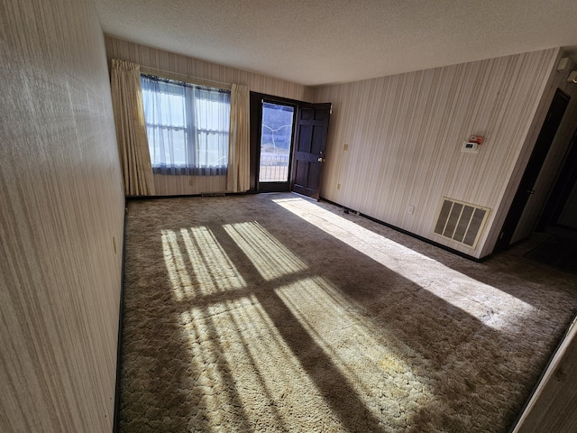 spare room featuring baseboards, visible vents, dark colored carpet, and a textured ceiling