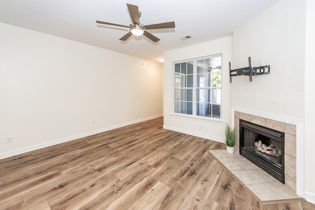 unfurnished living room with wood finished floors, a tile fireplace, baseboards, and a ceiling fan