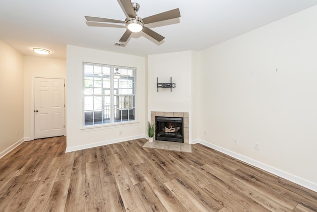 unfurnished living room featuring wood finished floors, a tile fireplace, ceiling fan, and baseboards