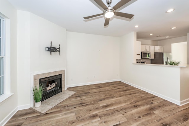 unfurnished living room featuring wood finished floors, ceiling fan, baseboards, recessed lighting, and a tiled fireplace