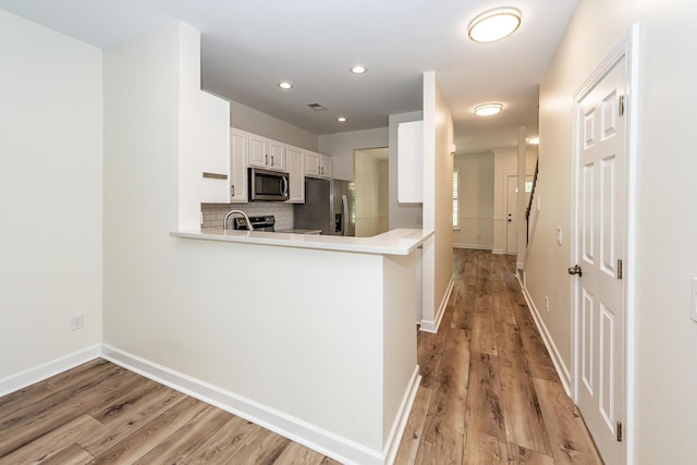 kitchen with stainless steel appliances, light wood-type flooring, a peninsula, baseboards, and recessed lighting
